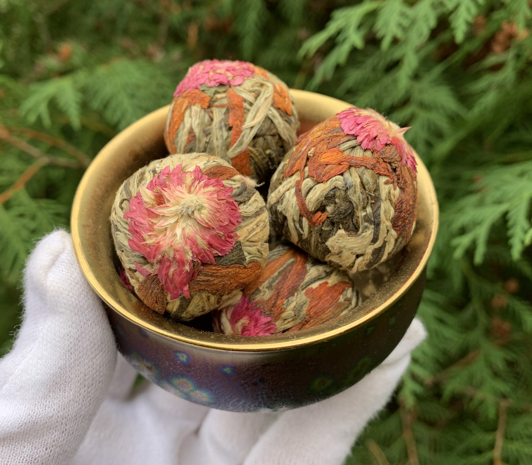 Hand in a white glove holding a brass bowl of flowering tea balls
